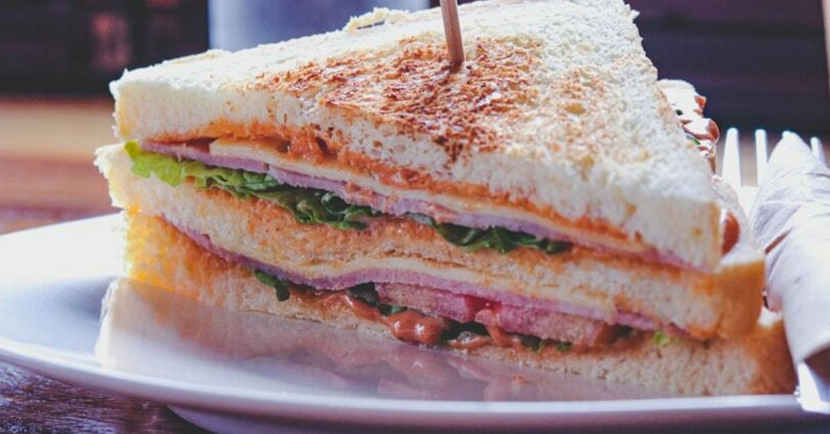 Enjoy a classic club sandwich, layered with turkey, bacon, lettuce, tomato, and mayo, stacked between toasted bread for a timeless favorite.